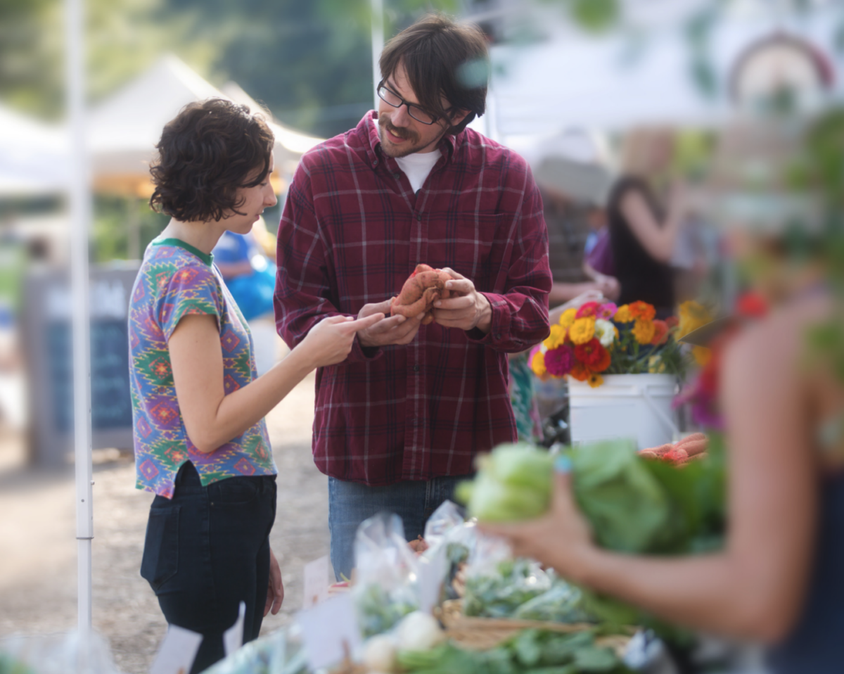 A man talking to a vendor at a farmer's market.